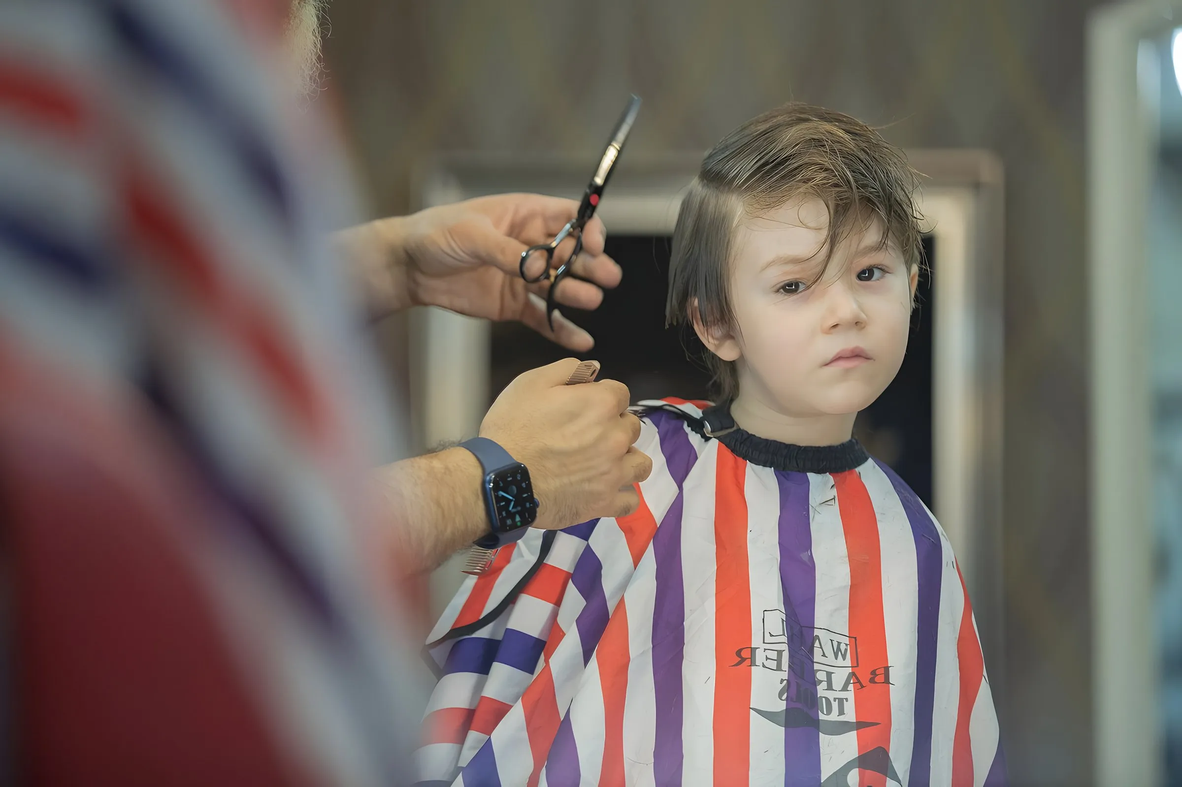 A young boy in a striped cape having his hair cut